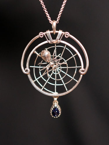 Silver pendant with spider and web design on a dark background