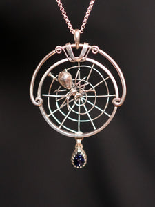 Silver pendant with spider and web design on a dark background